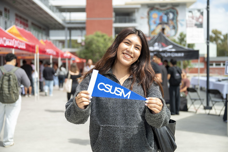 CSUSM Student with Pennant Student holding a CSUSM pennant at the San Diego City College University Transfer Fair.